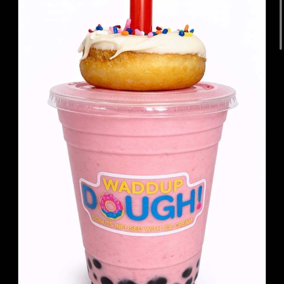 Strawberry boba shake with a white-frosted, sprinkle-covered donut on top, and a red straw.