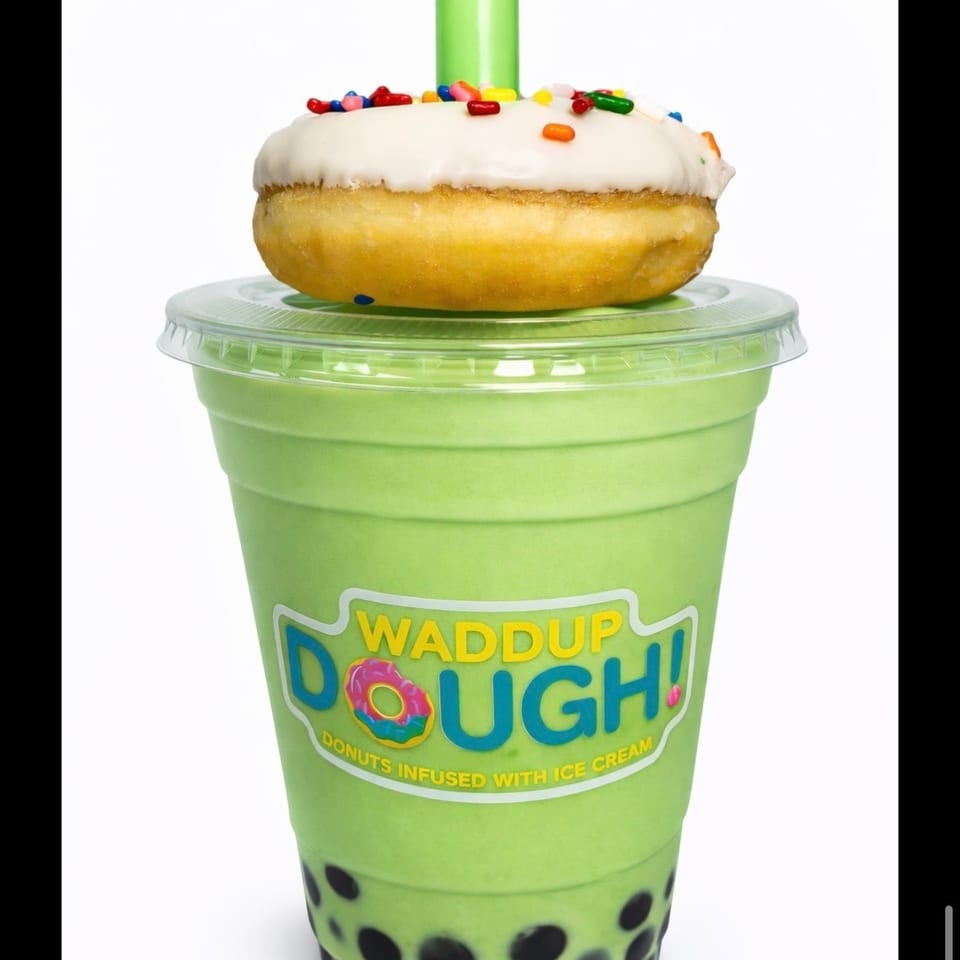 Honeydew boba shake with a white-frosted, sprinkle-covered donut on top, and a green straw.